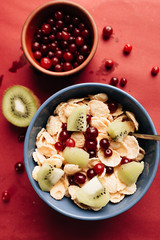 Delicious crispy cornflakes with kiwi pieces, almonds and cranberries in bowl, healthy breakfast on red background