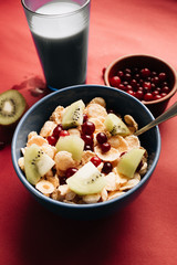 Delicious crispy cornflakes with kiwi pieces, almonds and cranberries in bowl, healthy breakfast on red background
