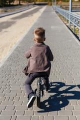 Happy four years old boy riding bicycle without pedals on the background of river and buildings. Sport concept. First balance bike for little children. Active and fun childhood outdoors