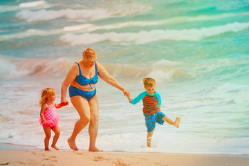 Happy grandmother with kids- little boy and girl- play on beach