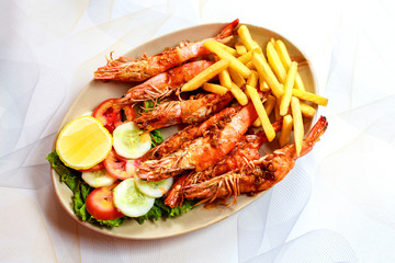 Plate grilled spicy prawn shrimps kebabs, vegetables, french fries with sauces and greens on light background.