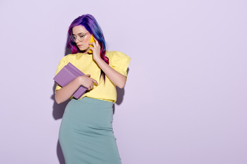 Fototapeta premium stylish young woman with colorful hair holding books and talking by phone on pink