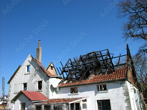 "Altes Bauernhaus mit ausgebranntem Dachstuhl vor azurblauem Himmel in