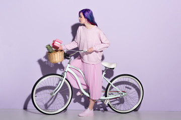beautiful young woman in pink clothing on bicycle with pineapple and gift box in basket