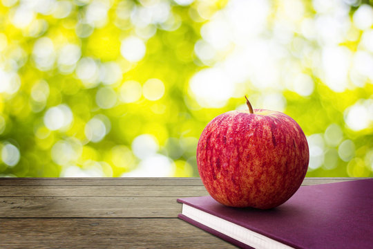 Red apples put on book with background Bokeh from the sun under the shade of trees.