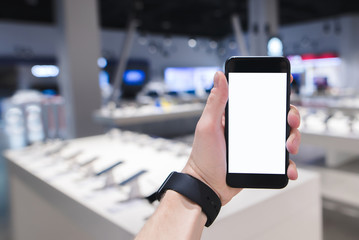 A person holds a smartphone in the background of a technology store. Phone against the background...