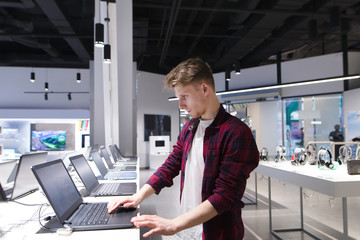 A young man chooses a laptop in an electronics store. A man looks at laptops in the computer department at the technology store. Buy a laptop