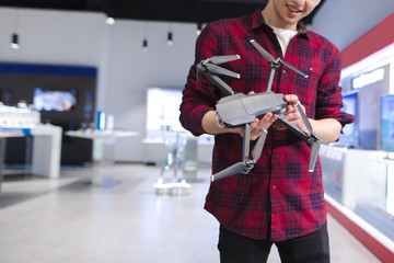 Portrait of a young man in a drones store. Quadcopter in the hands. A young man buys a drone in a tech store