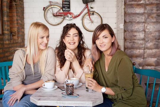 Photo of female friends drinking coffee together. Three young women at cafe smiling, laughing and having fun
