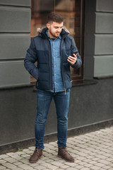 Handsome man in a jacket uses a phone standing on the street