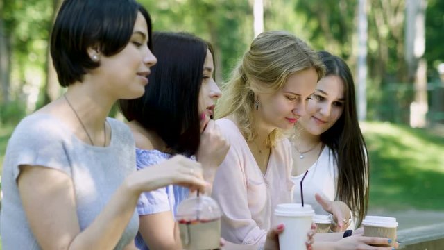 A group of friends drinking soft drinks and talking in the summer park. 4K