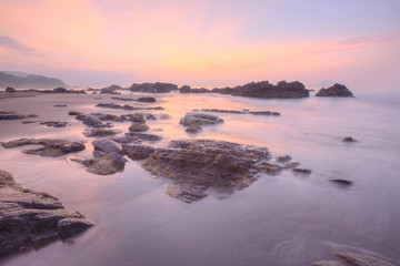 Fototapeta na wymiar Sunrise scenery of a beautiful rocky beach on northern coast of Taiwan with an island on distant horizon under dramatic dawning sky & golden sunlight reflecting on the seawater (Long Exposure Effect)
