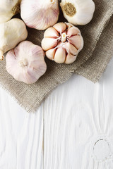 Garlic bulbs on canvas on white wood background.
