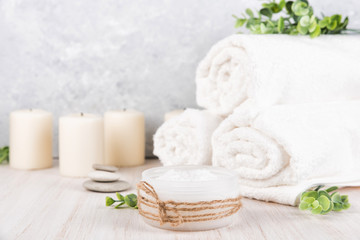 Fototapeta na wymiar Spa composition on white wooden background. Sea salt, white rolled towels, candles, green herbs