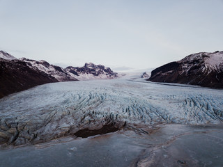 A glacier in Iceland with a frozen lake in front of it, shot with a drone