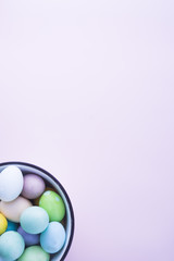 Colored eggs with pastelle tones inside a metallic bowl over a pink background, back lighted,  easter concept,holiday.