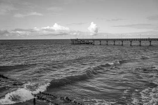 Fototapeta Seascape overlooking the long pier of the resort town with walking people.