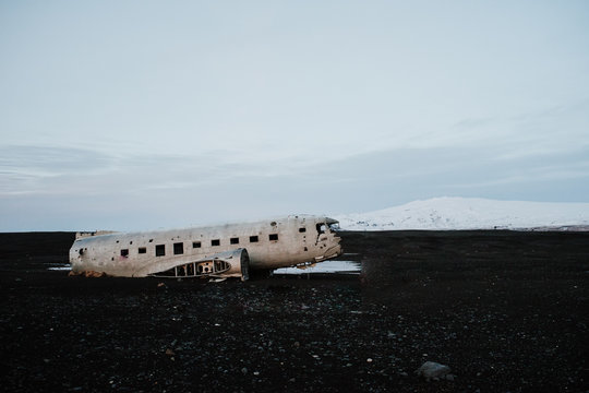 The famous plane wreck in Iceland in front of some mountains at a black sand beach.
