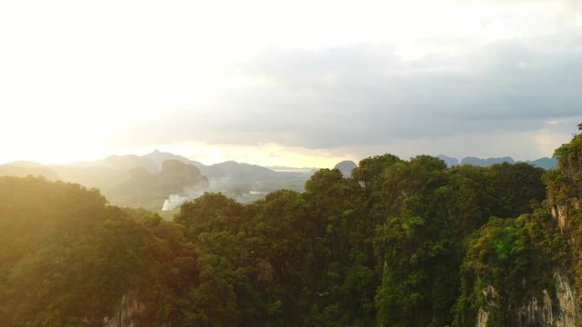 AERIAL. Cinematic style video of awesome landscape in Thailand. Rain clouds, mountains and green field view at the sunset. Camera moving slow from down to top and behind the mountain.