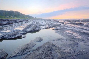 Dramatic sky  with reflections of golden sunlight on sea water and a distant island on horizon under dramatic dawning sky (Long Exposure Effect)~ Sunrise by the rocky coast in northern Taiwan 