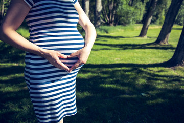 A pregnant woman showing a heart sign with her hands in the park.