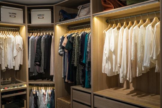 Luxury walk in closet / dressing room with lighting and jewel display. Dresses, handbags, blouses and sweaters on hangers in the wardrobes. Horizontal.