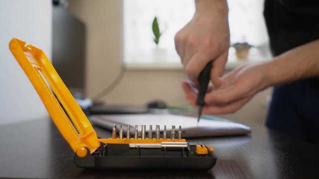 The wizard uses a screwdriver to twist the screw on the lid of the notebook.