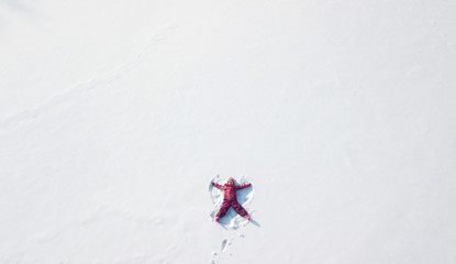Child girl playing and making a snow angel in the snow. Top flat overhead view