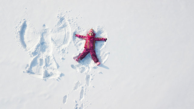 Child girl playing and making a snow angel in the snow. Top flat overhead view