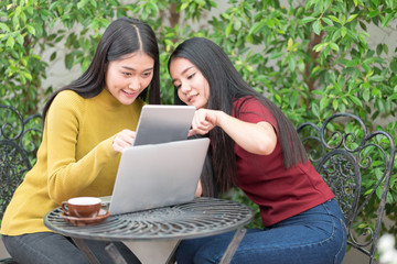 Two students teen girls studying together on line with a laptop in the garden with green tree background.