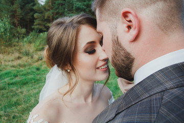 Fototapeta premium Beautiful wedding couple in the forest. The bride in tulle veil turns is smiling near the bearded groom in checkered suit. Rustic and stylish love story. Outdoors bridal portrait.