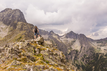 Surowy krajobraz górski, z ciemnymi chmurami. Kobieta obserwująca górską panoramę po wejściu na szczyt. Tatry Wysokie w Słowacji.
