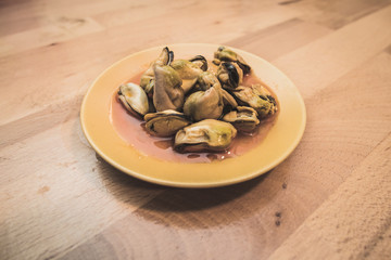 Typical spanish food of marinated mussels. They are on a small plate on a wooden table. 