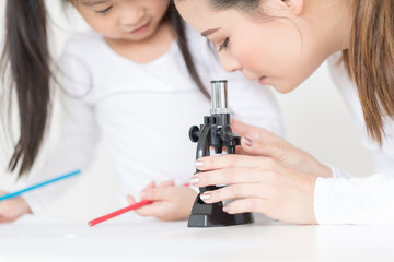 Mother and daughter are looking through a microscope. ther are doing some research.