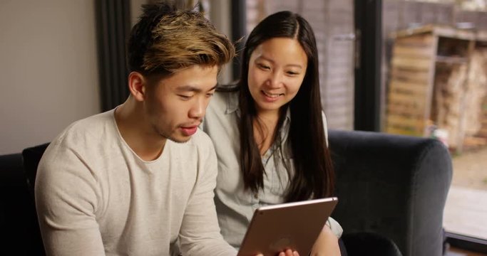 4K Cheerful couple relaxing at home, streaming media on a computer tablet