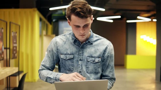 An attractive sexy young handsome guy with laptop in his hands walking somewhere, indoors footage, slow motion.