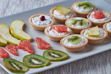 Tartlets with cream, cheese and fruits, cranberries, kiwi, apple, grapefruit.