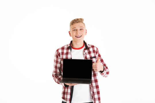 Teenager 18y wearing casual shirt holding silver notebook demonstrating or advertising copyspace screen and showing thumb up, isolated over white background