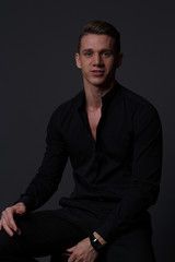 Fototapeta premium a guy in a black shirt and black pants sits on a dark chair, on a gray background
