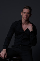 Fototapeta premium a guy in a black shirt and black pants sits on a dark chair, on a gray background