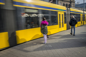 Passengers at the tram stop. Passengers are waiting to take off to the tram that arrives at the stop, blurred tram in the background.