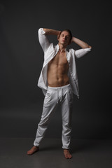 a guy with a naked torso, in white pants, and in a white shirt, stands on a gray background