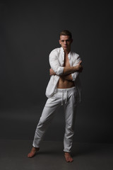 a guy with a naked torso, in white pants, and in a white shirt, stands on a gray background