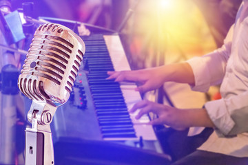 Close up retro microphone with musician playing keyboard synthesizer on band in night concert...