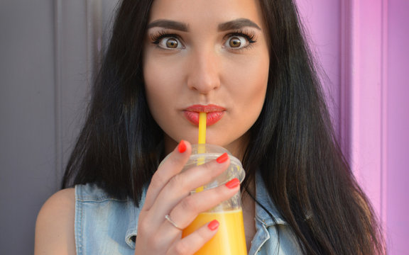Healthy lifestyle. The brunette girl drinks fresh juice through a straw. Widely open eyes. Orange fresh. Vitamins. Surprise. Close-up portrait. Delicious