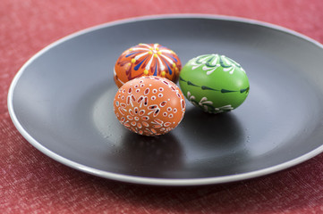 Group of wax painted Easter eggs spread on black plate, flower ornaments, traditional decoration