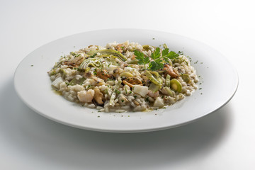 Round white dish of risotto with artichokes and seafood