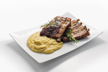 White rectangular plate with baked pork ribs and cornmeal mush