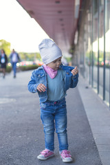 A little girl in jeans wear shows on the street