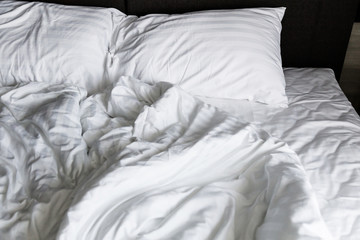 unmade rumpled bed with white messy pillows  in bedroom interior morning light